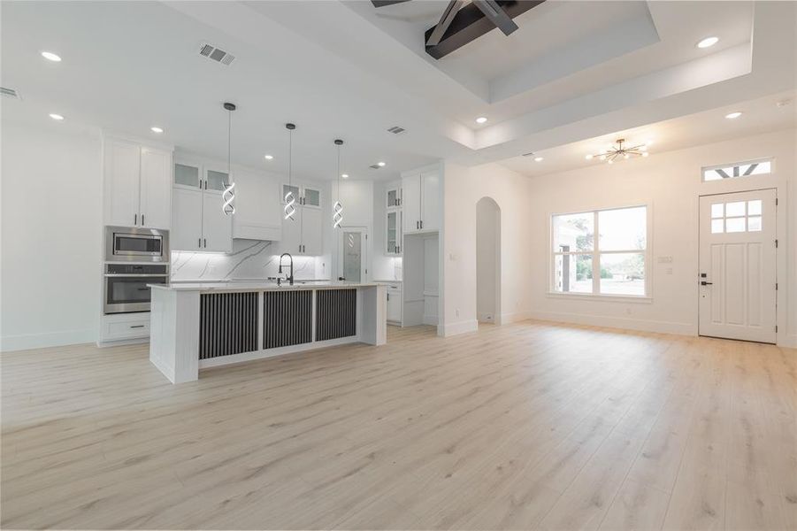 Kitchen with glass insert cabinets, a kitchen island with sink, white cabinets, open floor plan, and recessed lighting