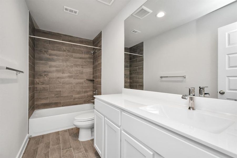 Secondary bath features tile flooring, bath/shower combo with tile surround, light stained wood cabinets, beautiful light countertop. Sample photo of completed home with similar floor plan. As-built interior colors and selections may vary.