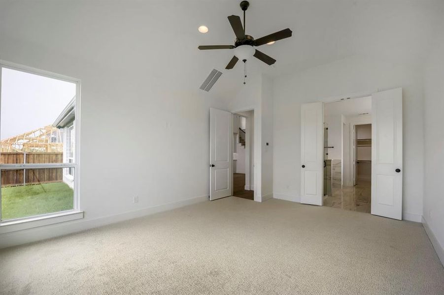 Spacious bedroom featuring light-colored carpeting, a large window, and a ceiling fan with integrated lighting Spacious bedroom featuring light-colored carpeting, a large window, and a ceiling fan with integrated lighting