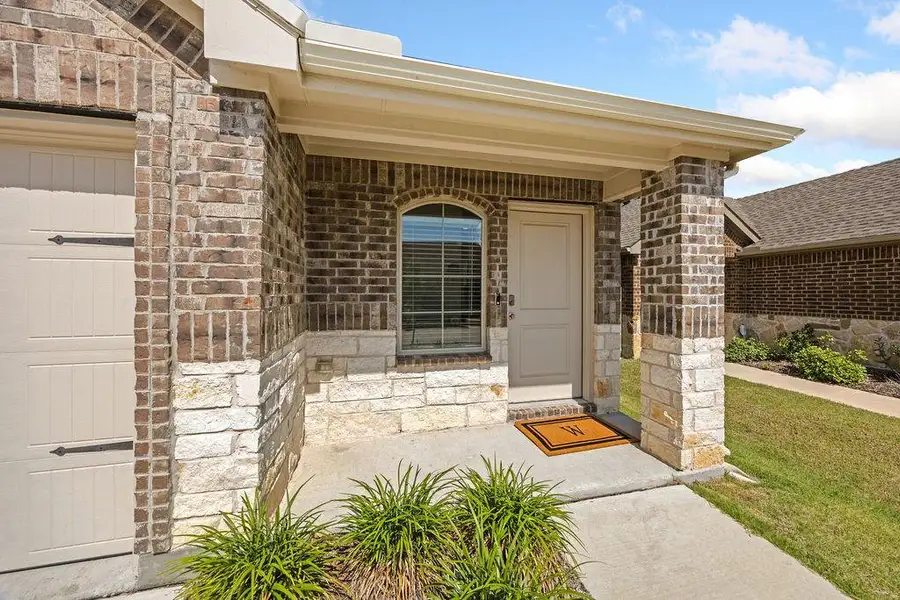 Welcoming covered entry featuring brick and stone veneer, an arched window, a paneled front door, and a concrete walkway Welcoming covered entry featuring brick and stone veneer, an arched window, a paneled front door, and a concrete walkway