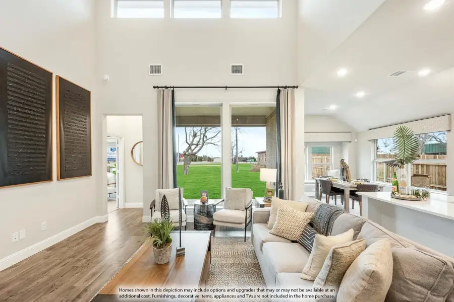 Open living room with two-story ceilings, hardwood floors, and large windows overlooking a green backyard