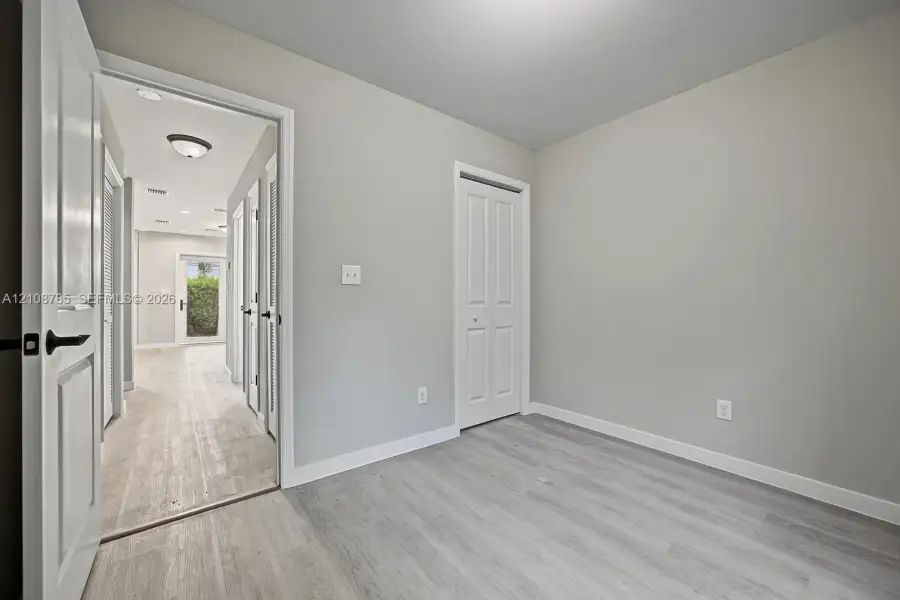 Interior space featuring neutral-toned walls, wood-finish flooring, and white paneled doors with matte black hardware Interior space featuring neutral-toned walls, wood-finish flooring, and white paneled doors with matte black hardware