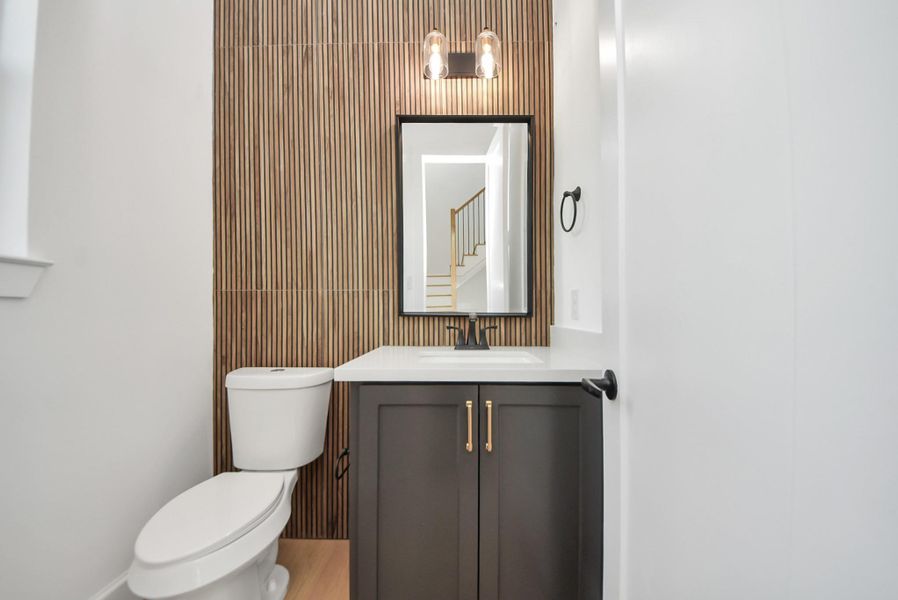 A modern bathroom accented by a warm wood-paneled feature wall, paired with a stylish vanity and gold hardware. Contemporary lighting above the mirror completes the refined look.