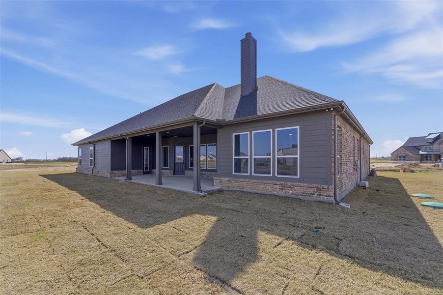 Back of house featuring a lawn, a chimney, and a patio area Back of house featuring a lawn, a chimney, and a patio area