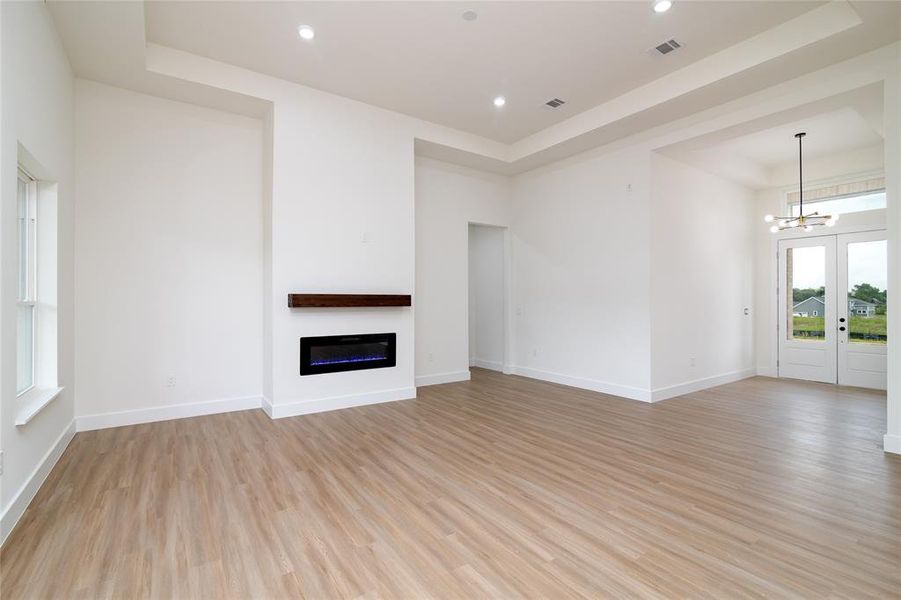 Unfurnished living room with a tray ceiling, light hardwood / wood-style flooring, and a chandelier