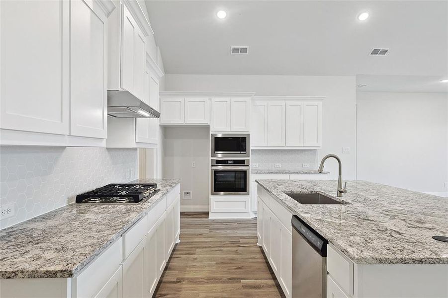 Kitchen featuring light wood-type flooring, sink, white cabinets, wall chimney range hood, and appliances with stainless steel finishes