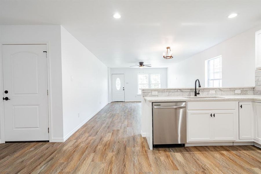 Kitchen featuring sink, light hardwood / wood-style floors, stainless steel dishwasher, white cabinetry, and ceiling fan