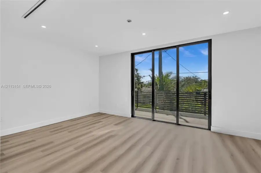 Room featuring wood-finish flooring, recessed lighting, and expansive floor-to-ceiling sliding glass doors opening to a balcony with horizontal slat railings Room featuring wood-finish flooring, recessed lighting, and expansive floor-to-ceiling sliding glass doors opening to a balcony with horizontal slat railings