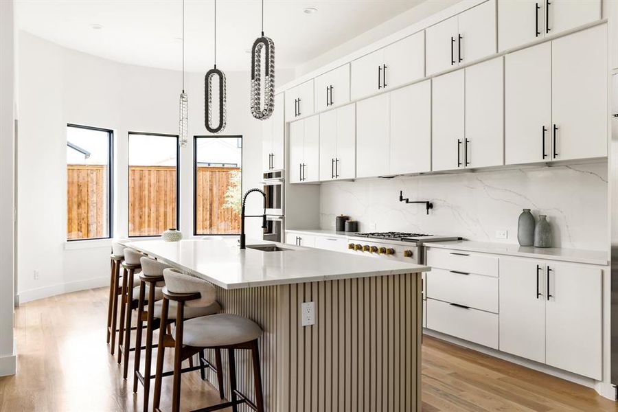 Kitchen with light wood-type flooring, decorative backsplash, a breakfast bar, hanging light fixtures, and a center island with sink Kitchen with light wood-type flooring, decorative backsplash, a breakfast bar, hanging light fixtures, and a center island with sink