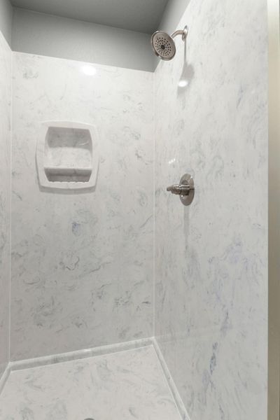 A well-lit shower stall features a clean, marbled surround and modern fixtures.