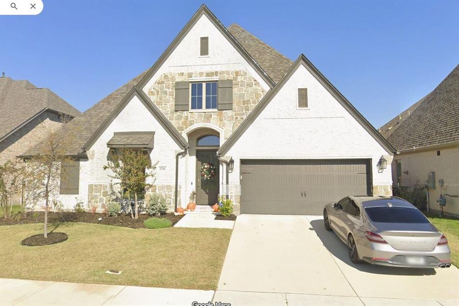 View of front of property featuring stone siding, a garage, driveway, brick siding, and a front lawn