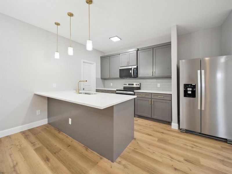 Kitchen featuring sink, hanging light fixtures, tasteful backsplash, appliances with stainless steel finishes, and light wood-type flooring