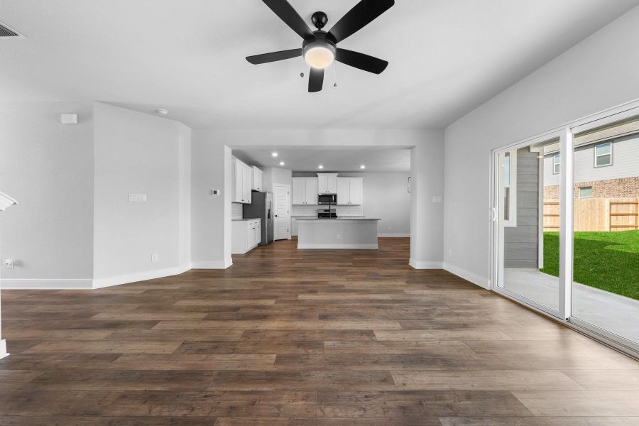 An open-concept interior features wood flooring, a ceiling fan, and sliding glass doors to the outside. An open-concept interior features wood flooring, a ceiling fan, and sliding glass doors to the outside.
