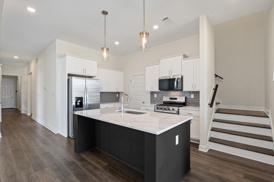 Kitchen featuring a dark-toned island with a light-toned countertop, stainless steel appliances, white cabinetry, and gray subway tile backsplash Kitchen featuring a dark-toned island with a light-toned countertop, stainless steel appliances, white cabinetry, and gray subway tile backsplash