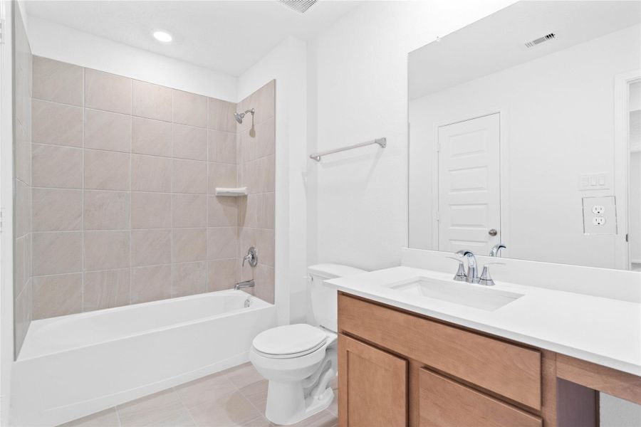 The secondary bathroom showcases tile flooring, a bath/shower combo with Daltile tile surround, a vanity with knee space, a stunning light countertop, a stylish mirror, sleek fixtures, and contemporary finishes throughout.