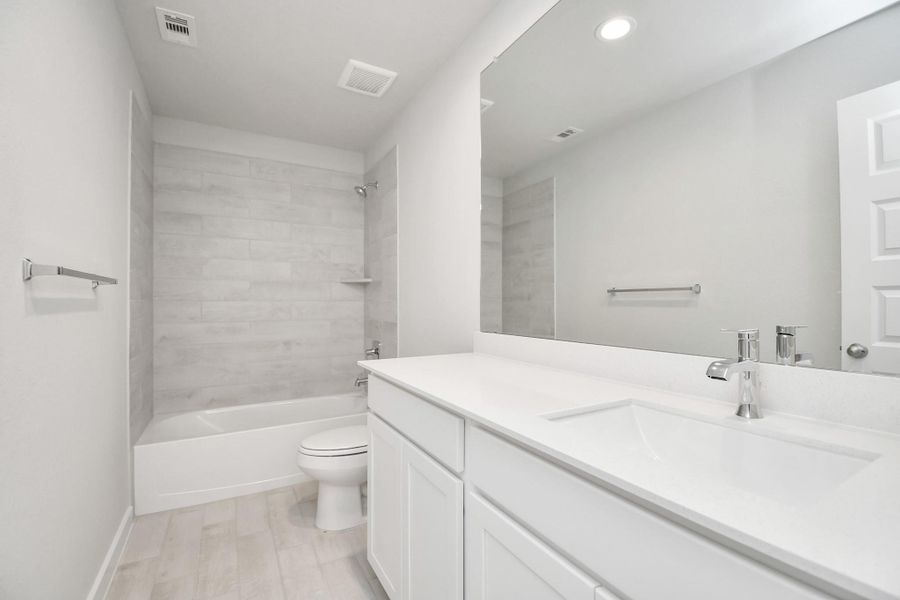 Secondary bath features tile flooring, bath/shower combo with tile surround, light stained wood cabinets, beautiful light countertop. Sample photo of completed home with similar floor plan. Actual colors and selections may vary.