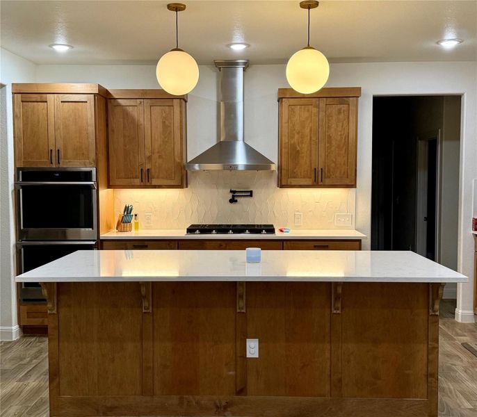 Kitchen featuring light wood finished floors, brown cabinetry, wall chimney exhaust hood, appliances with stainless steel finishes, and recessed lighting Kitchen featuring light wood finished floors, brown cabinetry, wall chimney exhaust hood, appliances with stainless steel finishes, and recessed lighting