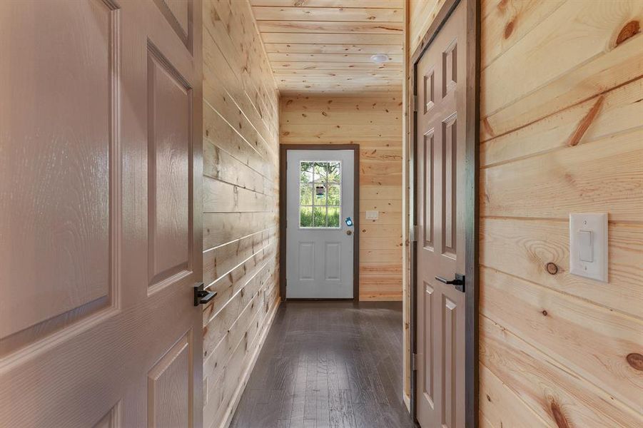 Doorway to outside featuring wood ceiling, wooden walls, and dark wood finished floors Doorway to outside featuring wood ceiling, wooden walls, and dark wood finished floors
