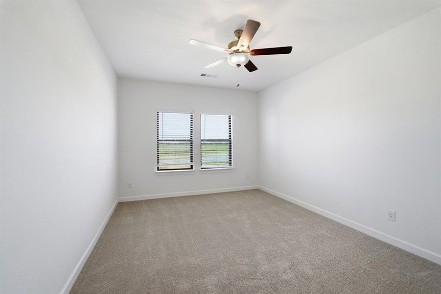 Bright room featuring neutral carpeting, a ceiling fan with integrated lighting, and two windows with blinds Bright room featuring neutral carpeting, a ceiling fan with integrated lighting, and two windows with blinds