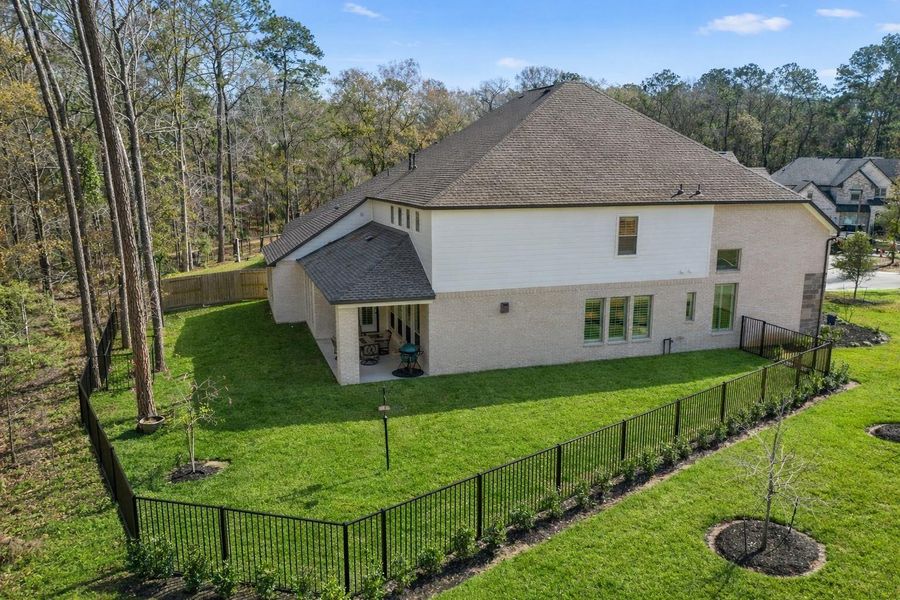 This photo showcases a spacious two-story home with a fenced backyard, bordered by a serene wooded area. The property features a well-maintained lawn and a covered patio, perfect for outdoor relaxation. Ideal for those seeking privacy and a connection to nature.