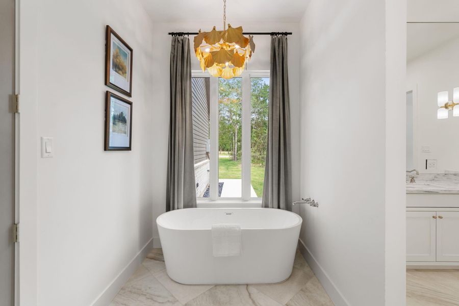 Freestanding soaking tub perfectly positioned beneath tall windows that bring in natural light and peaceful backyard views. Clean lines and minimalist finishes give this space a calm, retreat-like feel. The private tub alcove offers a quiet spot to unwind, complemented by refined tilework and elevated lighting overhead.