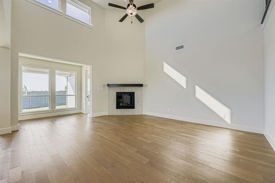 Unfurnished living room featuring a towering ceiling, ceiling fan, light wood-style floors, and a tiled fireplace