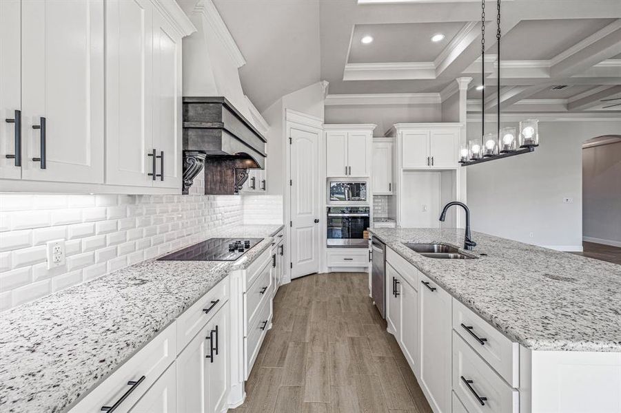 Kitchen featuring tasteful backsplash, light stone countertops, a kitchen island with sink, appliances with stainless steel finishes, and coffered ceiling