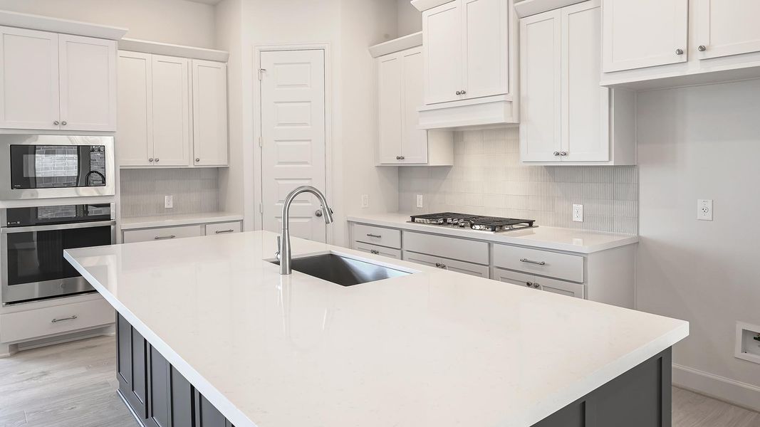 Kitchen with stainless steel appliances, white cabinets, decorative backsplash, and light stone countertops