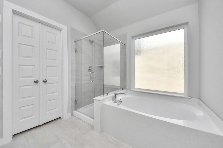 Indulge in a spa-like retreat within the confines of this primary bathroom. Delight in a spacious walk-in shower enveloped in stylish tile surround, unwind in a separate garden tub adorned with custom detailing. Sample photo of completed home with similar floor plan. Actual colors and selections may vary.