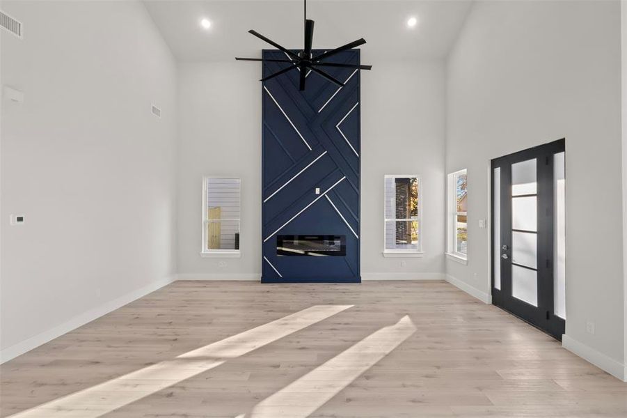 Unfurnished living room with a high ceiling, light wood-type flooring, and ceiling fan