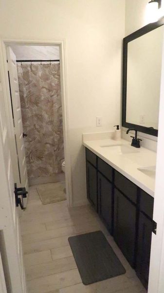 This additional full bathroom features a modern design with a double-sink vanity, dark cabinetry, and a large mirror. The neutral color palette is complemented by a patterned shower curtain, creating a clean and inviting space. This additional full bathroom features a modern design with a double-sink vanity, dark cabinetry, and a large mirror. The neutral color palette is complemented by a patterned shower curtain, creating a clean and inviting space.