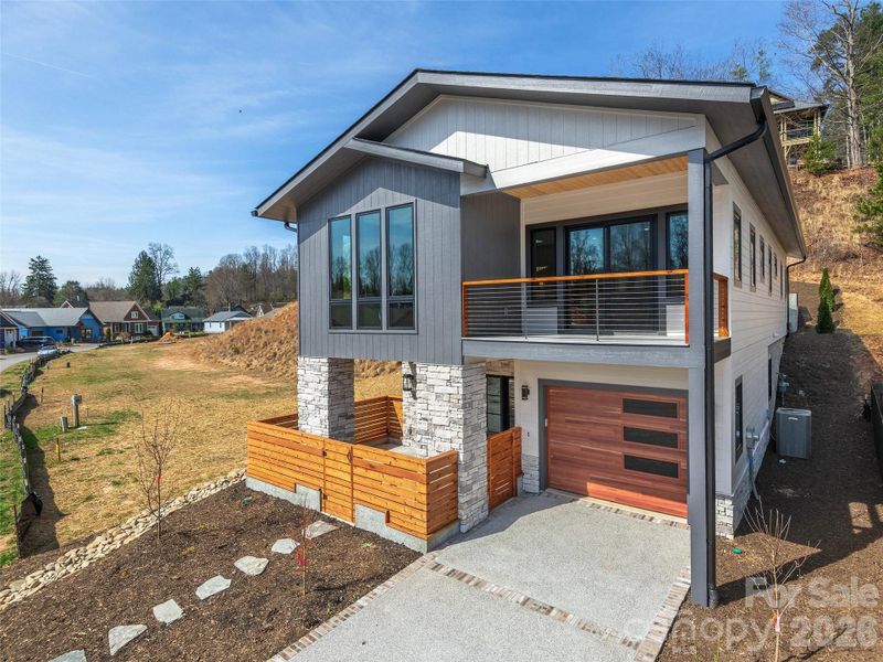 Front exterior of the completed Courtyard Villa showcasing modern mountain architecture, cultured stone accents, covered upper-level porch, private entry courtyard, and attached garage.