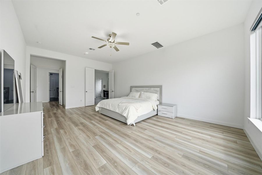Spacious room featuring light-colored flooring, a ceiling fan, and large windows providing natural light
