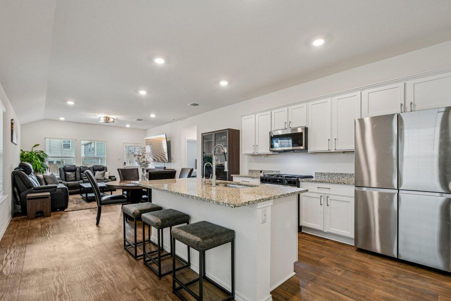 Kitchen with stainless steel appliances, white cabinets, light stone countertops, open floor plan, and dark wood-type flooring