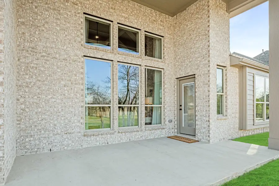 Covered back patio with concrete floor, light brick exterior, large windows, and glass door with welcome mat Covered back patio with concrete floor, light brick exterior, large windows, and glass door with welcome mat
