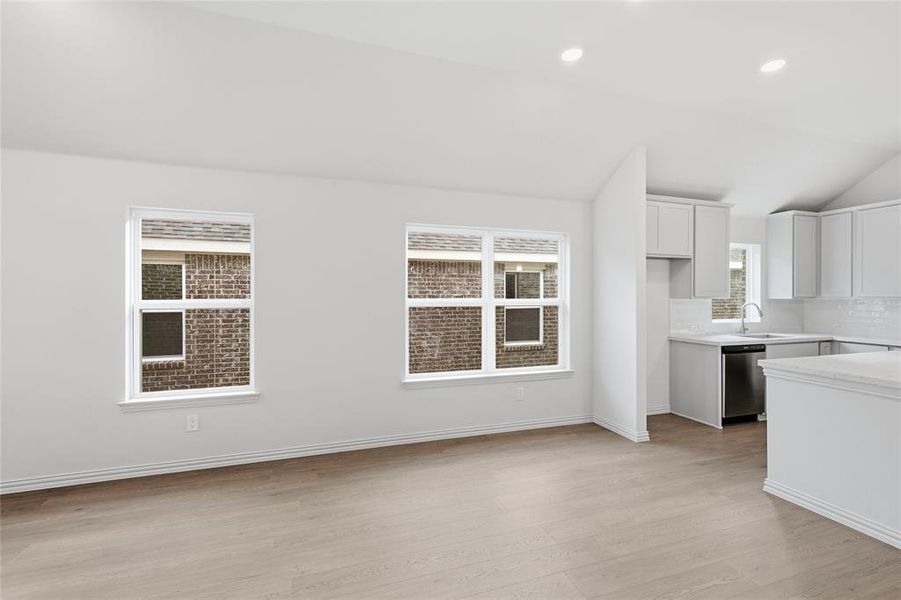 Kitchen featuring white cabinetry, light wood-type flooring, recessed lighting, vaulted ceiling, and stainless steel dishwasher