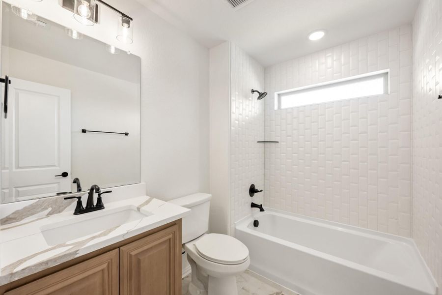 Bathroom with wood vanity, marble countertop, white subway tile tub surround, and matte black fixtures