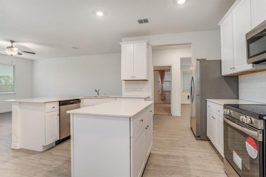 Kitchen with stainless steel appliances, a kitchen island, white cabinetry, a ceiling fan, and a peninsula