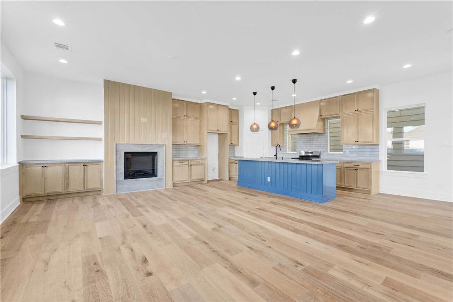 Second-floor main living and kitchen area with abundant natural light, high ceilings, engineered wood floors, custom built-ins, and a stunning custom fireplace as the focal point. Features an oversized island with Taj Mahal quartzite countertops and integrated appliances.