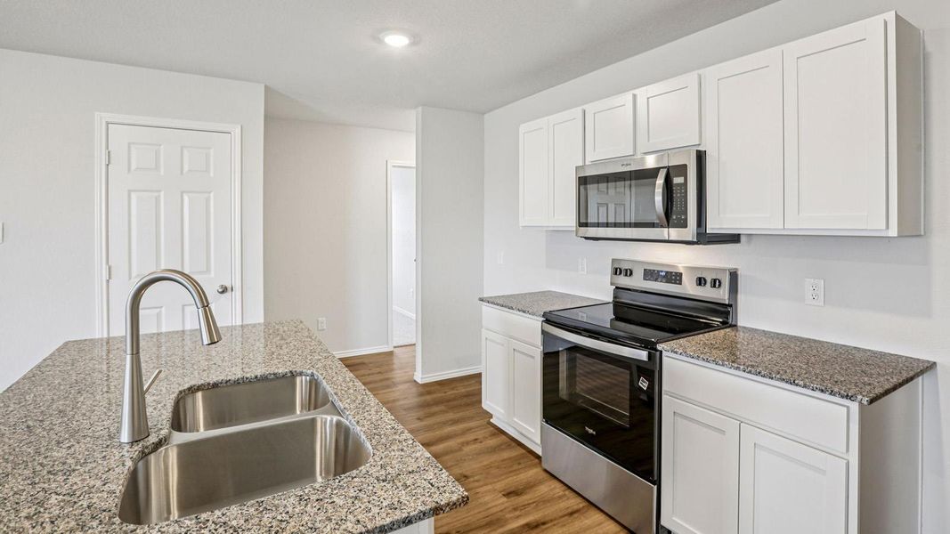 Kitchen featuring wood-finish flooring, white cabinetry, speckled countertops, stainless steel appliances, and a double basin sink with a pull-down faucet Kitchen featuring wood-finish flooring, white cabinetry, speckled countertops, stainless steel appliances, and a double basin sink with a pull-down faucet