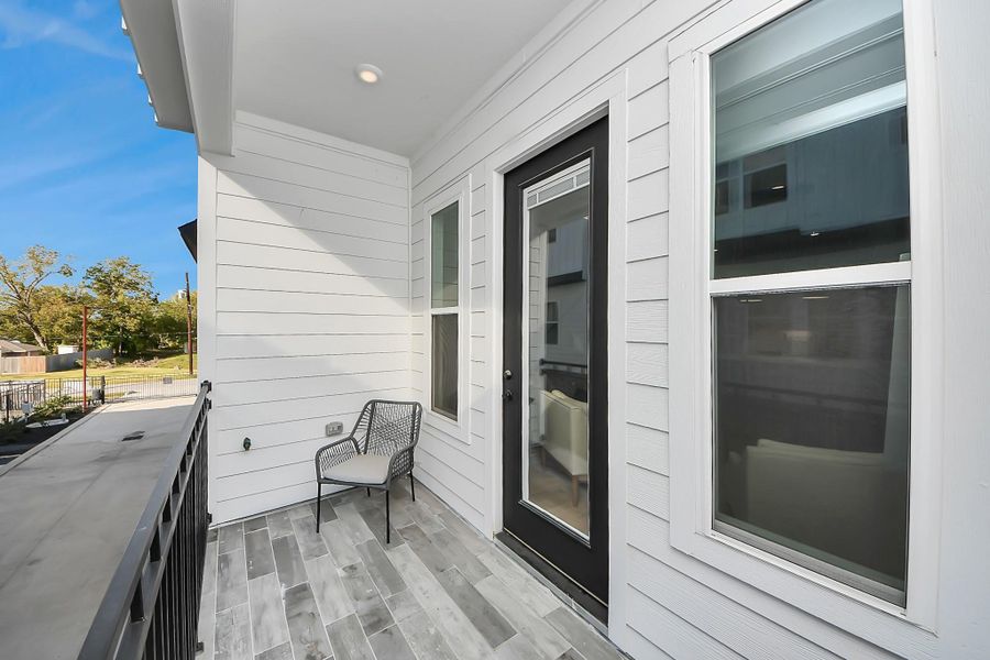 This photo showcases a modern, cozy balcony with white siding and wood-look tile flooring. It features a black-framed glass door and windows, offering plenty of natural light. An inviting space for relaxation.