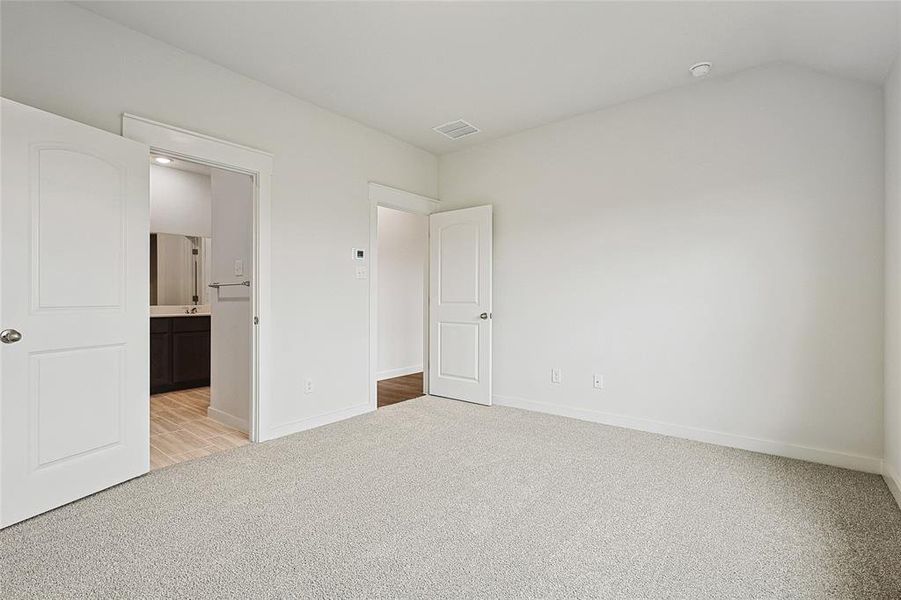 Unfurnished bedroom featuring connected bathroom, lofted ceiling, and light colored carpet