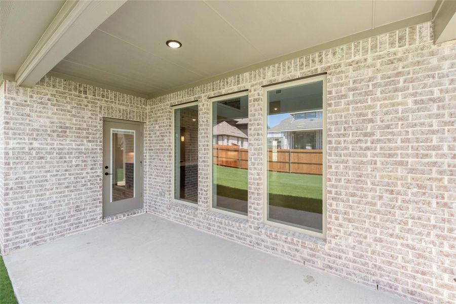 Covered back patio with concrete floor, light brick exterior, back door, and large windows overlooking fenced yard Covered back patio with concrete floor, light brick exterior, back door, and large windows overlooking fenced yard