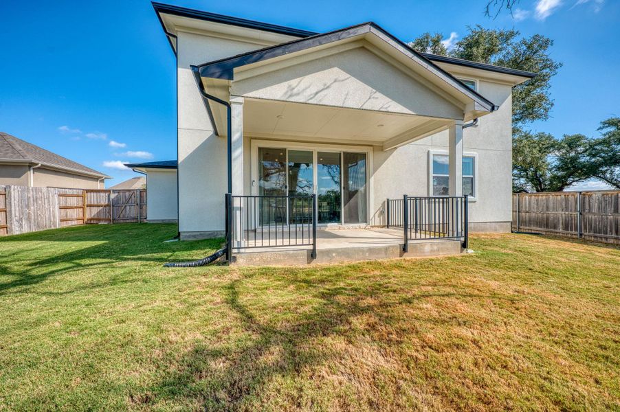 A covered back porch overlooks a fenced grassy yard under clear blue skies. A covered back porch overlooks a fenced grassy yard under clear blue skies.