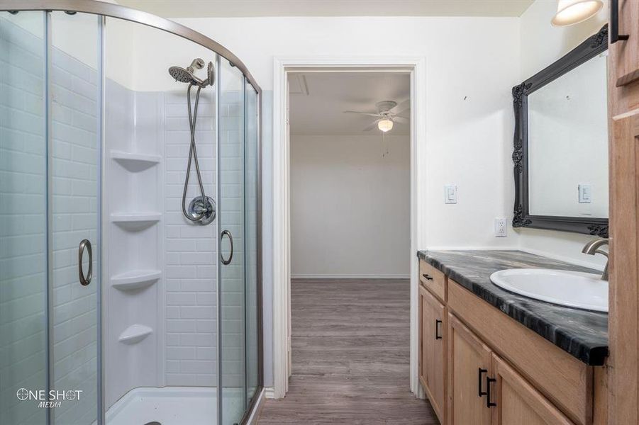 Bathroom featuring walk in shower, hardwood / wood-style flooring, vanity, and ceiling fan