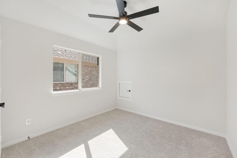 Empty bedroom with vaulted ceiling, black ceiling fan, carpet flooring, and a single window Empty bedroom with vaulted ceiling, black ceiling fan, carpet flooring, and a single window