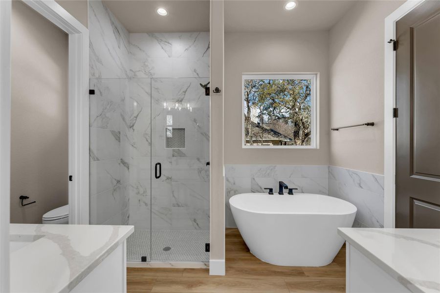 Bathroom featuring vanity, a marble finish shower, a soaking tub, tile walls, and a wainscoted wall