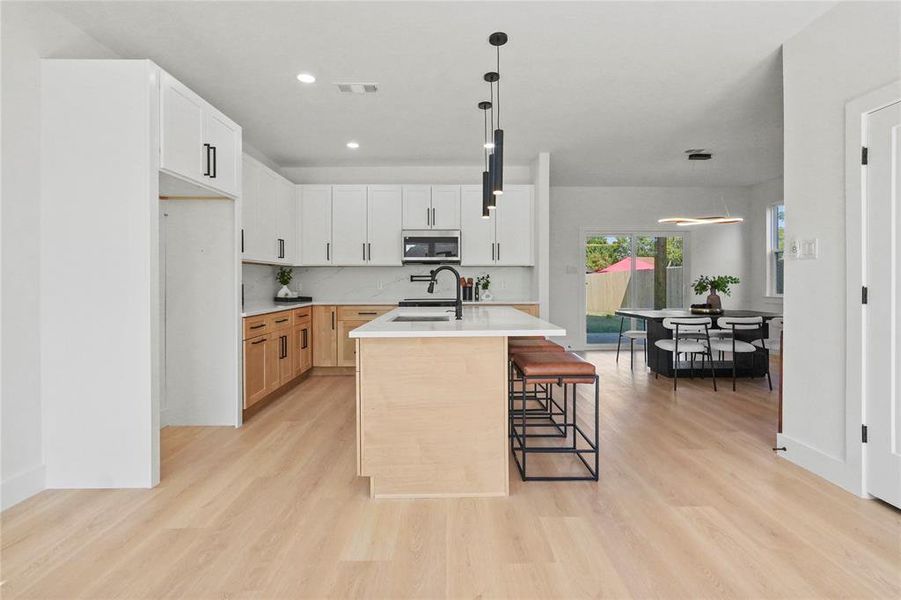 Kitchen featuring white cabinetry, backsplash, light wood finished floors, decorative light fixtures, and recessed lighting Kitchen featuring white cabinetry, backsplash, light wood finished floors, decorative light fixtures, and recessed lighting
