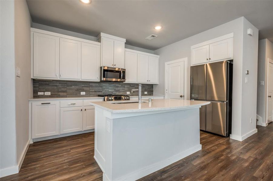 Kitchen featuring dark wood-style floors, stainless steel appliances, decorative backsplash, light countertops, and white cabinets