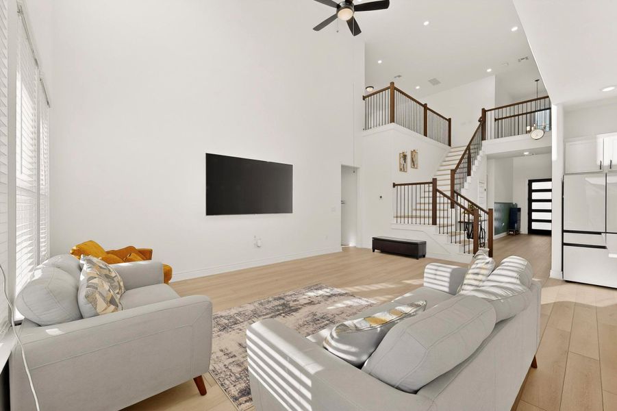 Living room featuring light wood-style flooring, stairs, a ceiling fan, and a towering ceiling